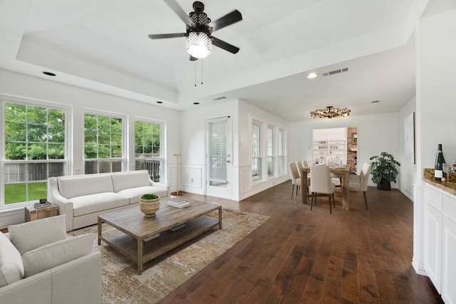 living room with ceiling fan, dark wood-type flooring, and a tray ceiling