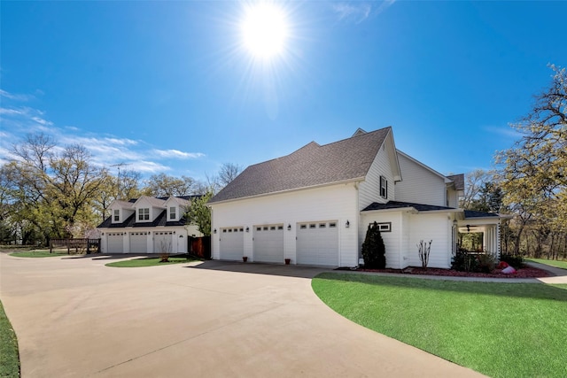 view of side of property with driveway, an attached garage, a lawn, and roof with shingles