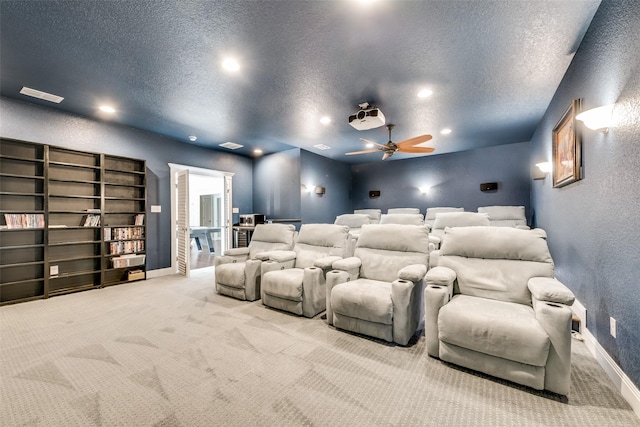 home theater room featuring ceiling fan, light colored carpet, and a textured ceiling