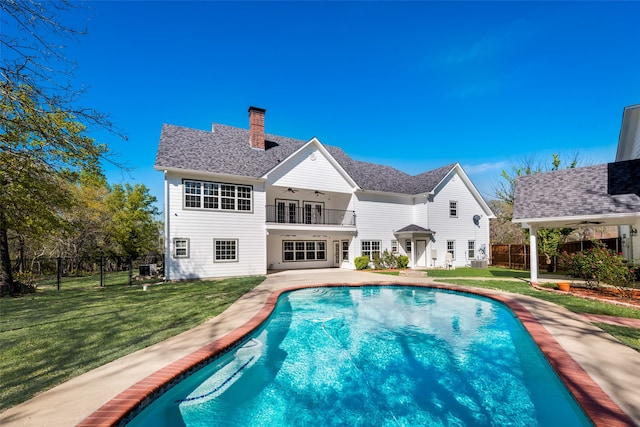 back of house featuring a balcony, a fenced in pool, a lawn, and ceiling fan