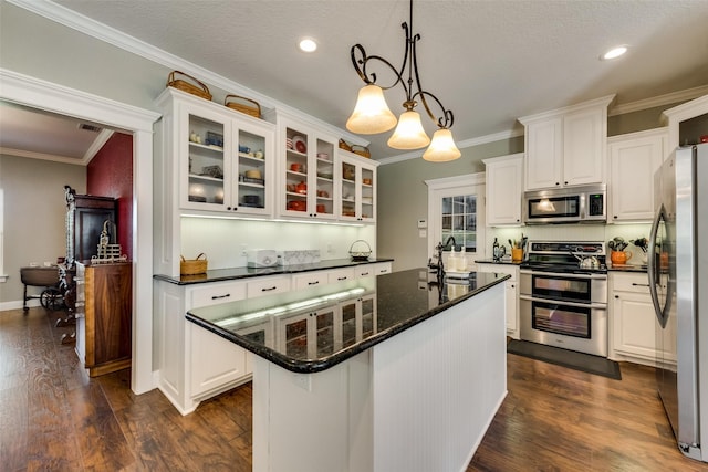 kitchen featuring crown molding, white cabinetry, hanging light fixtures, appliances with stainless steel finishes, and an island with sink