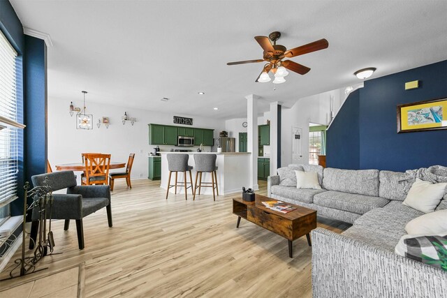 living room featuring a wealth of natural light, ceiling fan, decorative columns, and light wood-type flooring