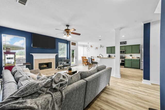 living room featuring ceiling fan, sink, a tiled fireplace, and light hardwood / wood-style floors