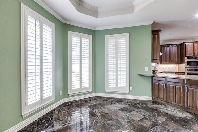 kitchen with a raised ceiling, ornamental molding, light stone counters, and double oven