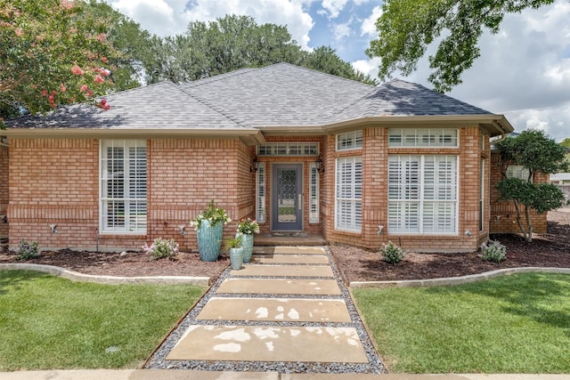 view of front of property featuring a shingled roof, brick siding, and a front lawn