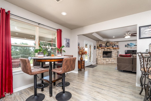 dining room with ceiling fan, a stone fireplace, and light hardwood / wood-style floors