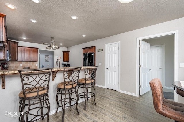 kitchen with a textured ceiling, a kitchen bar, black refrigerator, backsplash, and hanging light fixtures