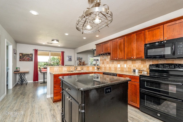 kitchen with black appliances, a center island, dark stone counters, sink, and light hardwood / wood-style flooring