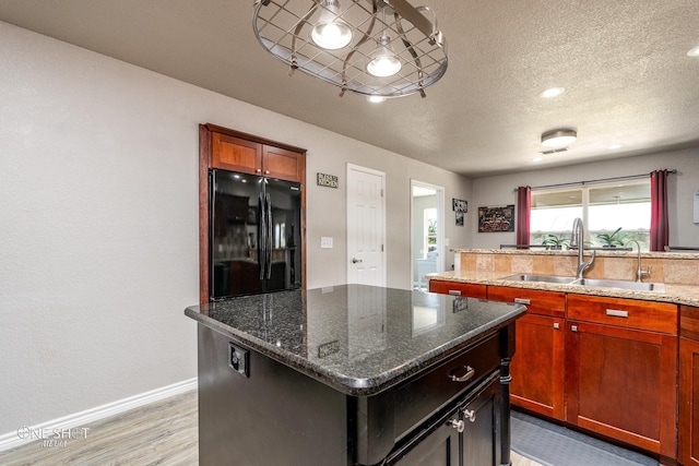 kitchen featuring a center island, dark stone counters, sink, black fridge, and light wood-type flooring