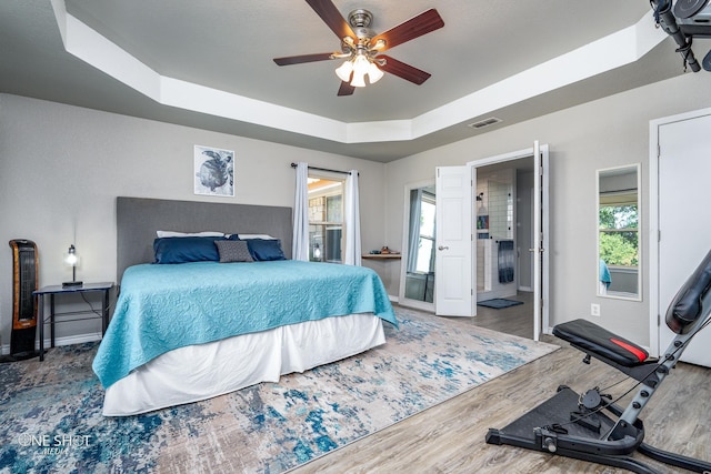 bedroom featuring ceiling fan, multiple windows, wood-type flooring, and a tray ceiling