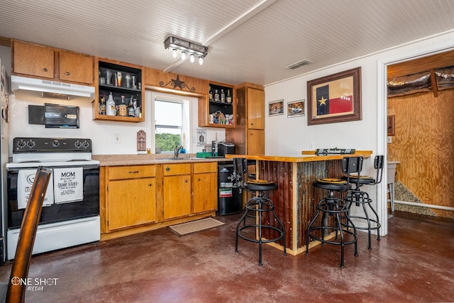 kitchen with sink, white electric stove, wooden walls, and a breakfast bar area