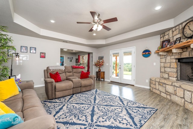 living room with a raised ceiling, ceiling fan, a fireplace, and hardwood / wood-style floors