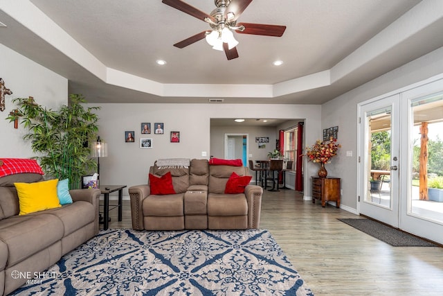 living room featuring a raised ceiling, ceiling fan, and light hardwood / wood-style flooring