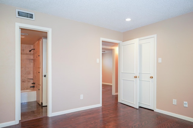 unfurnished bedroom with dark wood-type flooring, a textured ceiling, and ensuite bathroom