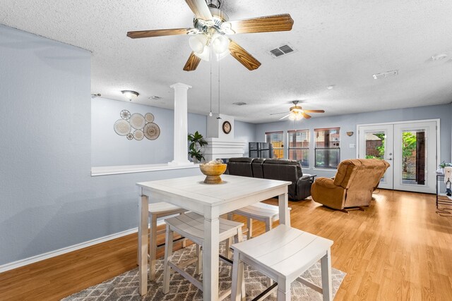 dining space with light wood-type flooring, ornate columns, and a textured ceiling