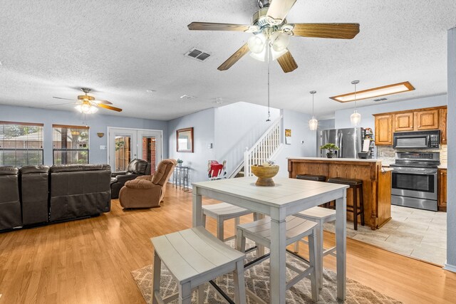 dining area with ceiling fan, light wood-type flooring, and a textured ceiling