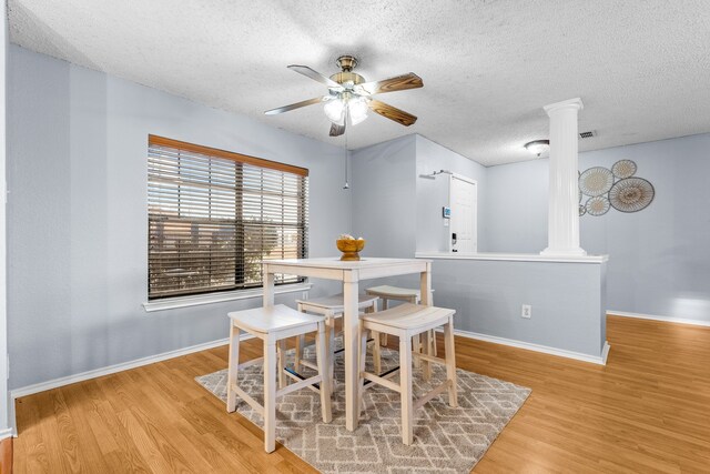 dining space featuring ceiling fan, a textured ceiling, light hardwood / wood-style floors, and decorative columns