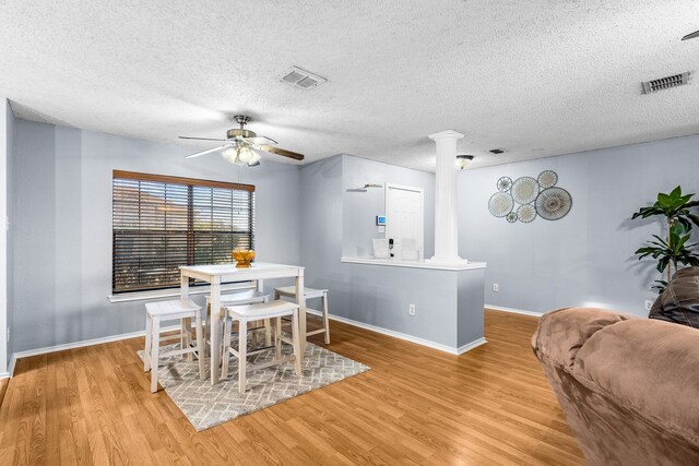 dining area with decorative columns, light hardwood / wood-style floors, a textured ceiling, and ceiling fan