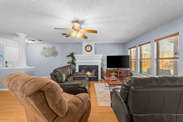 living room featuring ceiling fan, light hardwood / wood-style floors, a textured ceiling, a high end fireplace, and ornate columns