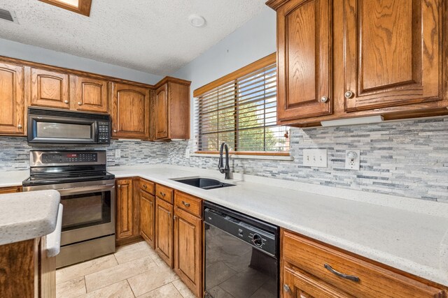 kitchen featuring tasteful backsplash, light tile patterned flooring, a textured ceiling, black appliances, and sink