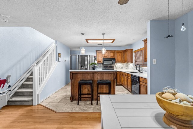 kitchen with a kitchen island, black appliances, decorative backsplash, sink, and light hardwood / wood-style flooring