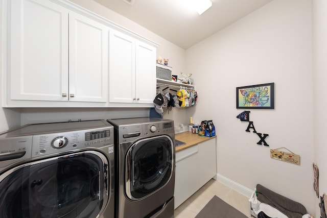 clothes washing area featuring washer and dryer, light tile patterned floors, and cabinets