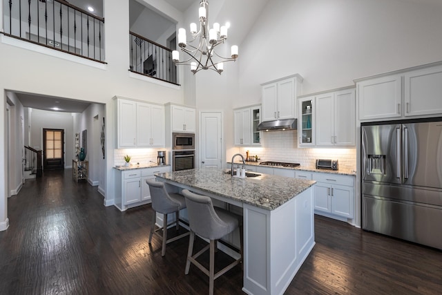 kitchen featuring a towering ceiling, an island with sink, white cabinets, and appliances with stainless steel finishes