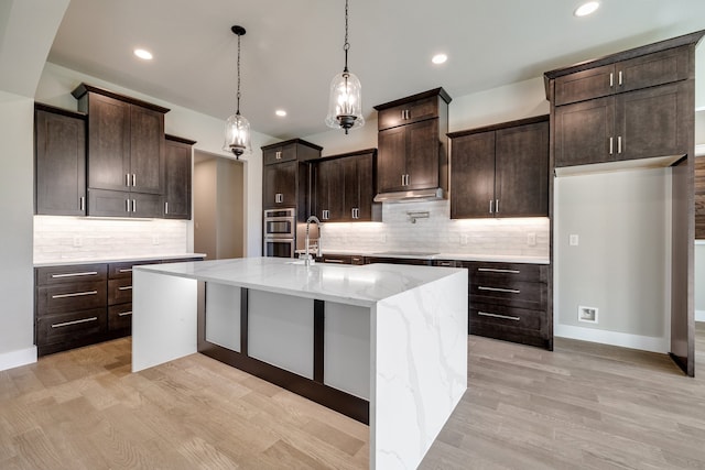 kitchen featuring tasteful backsplash, light wood-type flooring, and an island with sink