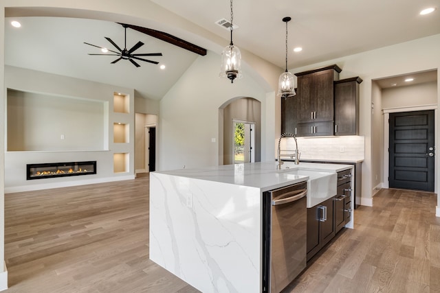 kitchen with light stone countertops, sink, light wood-type flooring, lofted ceiling with beams, and a kitchen island with sink