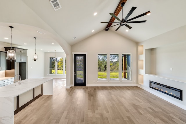 unfurnished living room featuring a healthy amount of sunlight, beamed ceiling, and light wood-type flooring