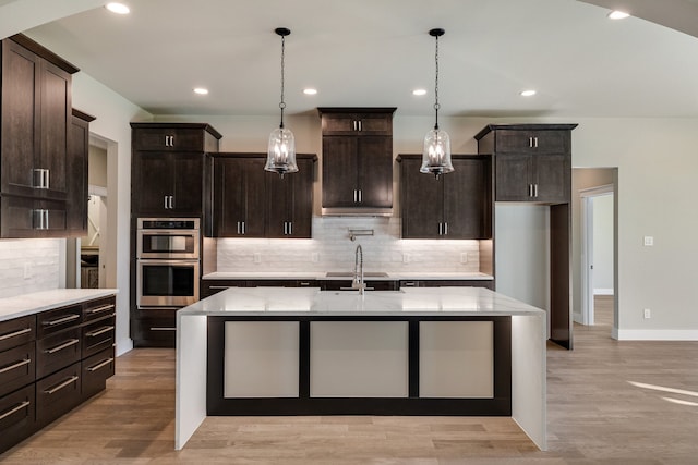 kitchen with light hardwood / wood-style floors, dark brown cabinets, a center island with sink, and stainless steel double oven