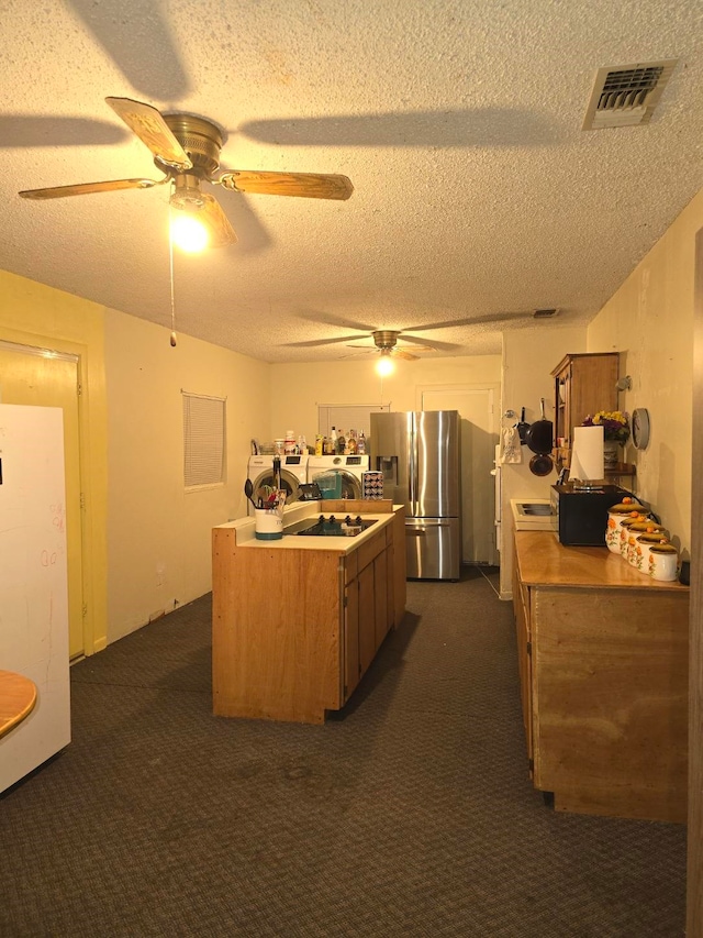 kitchen featuring washer and clothes dryer, dark colored carpet, stainless steel fridge, a textured ceiling, and ceiling fan