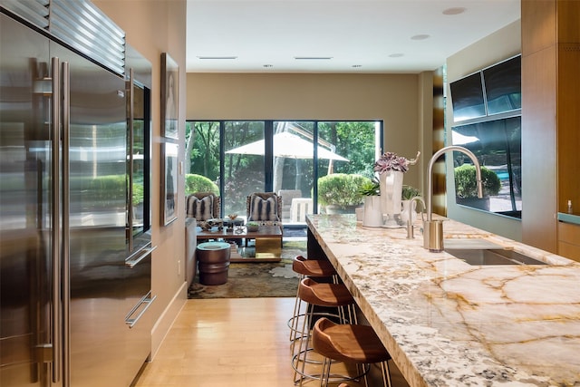 kitchen with a kitchen bar, sink, light hardwood / wood-style flooring, high end fridge, and light stone countertops