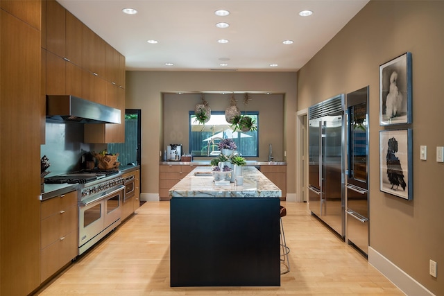 kitchen featuring range hood, a kitchen island, a breakfast bar, light hardwood / wood-style flooring, and high quality appliances