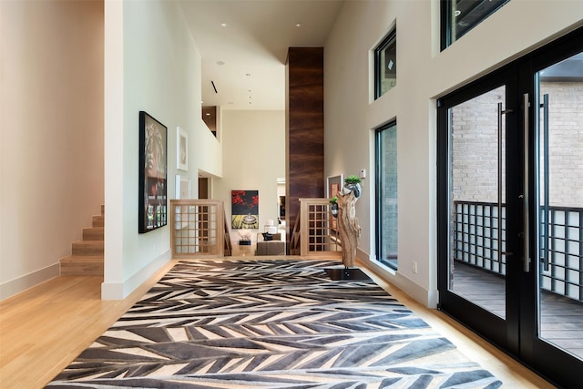 corridor with french doors, a towering ceiling, and wood-type flooring