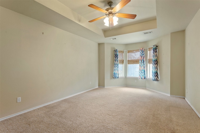 empty room with a raised ceiling, carpet floors, and ceiling fan