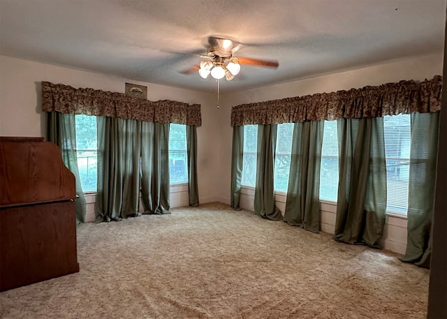 carpeted spare room featuring a healthy amount of sunlight and ceiling fan