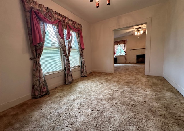 empty room featuring a brick fireplace, light colored carpet, and ceiling fan