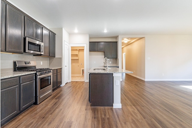 kitchen featuring stainless steel appliances, dark brown cabinetry, light stone counters, and tasteful backsplash