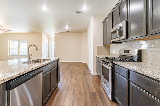 kitchen with sink, dark brown cabinetry, stainless steel appliances, dark hardwood / wood-style flooring, and light stone counters