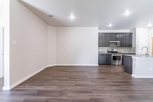 kitchen with appliances with stainless steel finishes, dark hardwood / wood-style floors, light stone counters, dark brown cabinetry, and sink