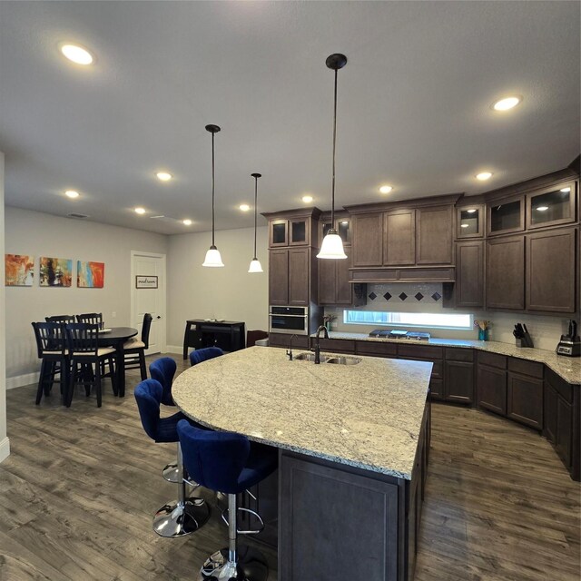 kitchen with stainless steel appliances, a center island with sink, sink, pendant lighting, and dark hardwood / wood-style floors