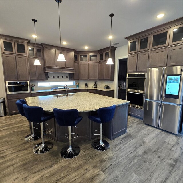 kitchen with a center island with sink, pendant lighting, appliances with stainless steel finishes, and light wood-type flooring