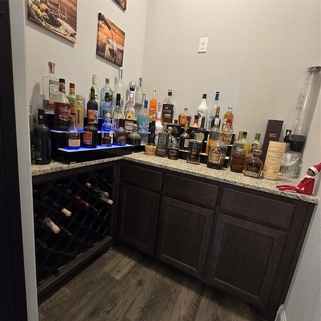 bar with dark hardwood / wood-style flooring, light stone counters, and dark brown cabinetry