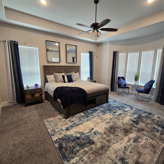 carpeted bedroom with a tray ceiling, multiple windows, and ceiling fan