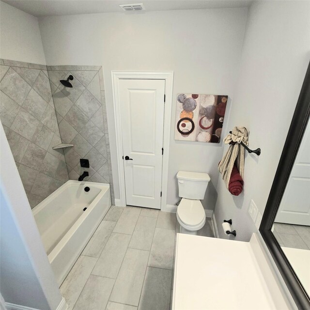 bathroom featuring tile patterned flooring, toilet, and tiled shower / bath