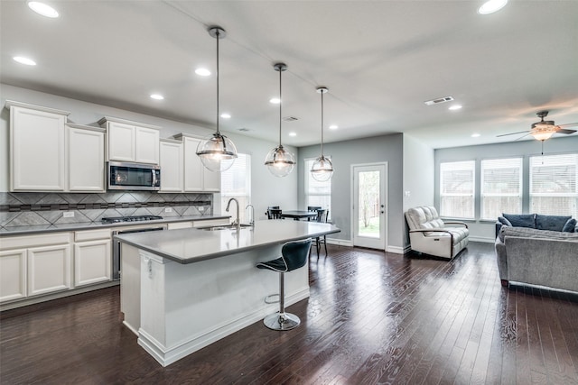 kitchen with sink, appliances with stainless steel finishes, white cabinets, a center island with sink, and decorative light fixtures