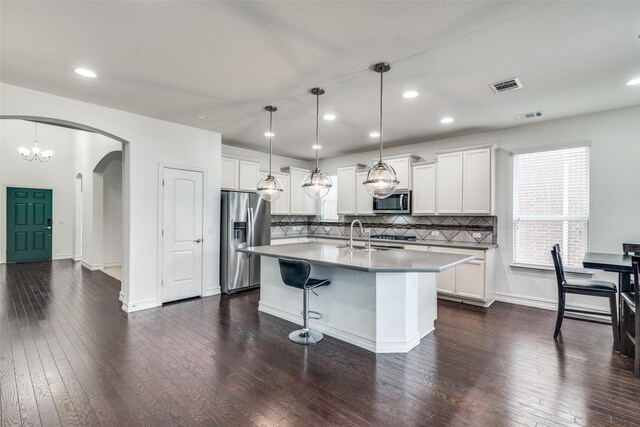 kitchen featuring backsplash, appliances with stainless steel finishes, dark hardwood / wood-style flooring, and a center island with sink