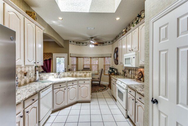 kitchen with a skylight, sink, kitchen peninsula, white appliances, and ceiling fan