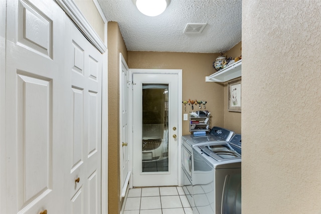 clothes washing area featuring washing machine and clothes dryer, a textured ceiling, and light tile patterned flooring